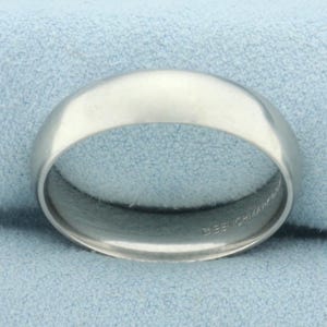 May include: A silver wedding band with a smooth, polished finish. The inside of the band is engraved with "18K CHIAMPA".