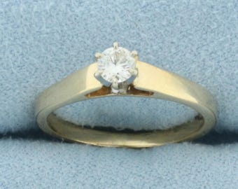 May include: A simple gold band engagement ring with a single round diamond.