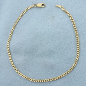 May include: A yellow gold curb chain bracelet featuring a series of interlocking, flattened oval links. The bracelet is finished with a secure lobster claw clasp mechanism at one end, allowing for easy fastening and removal of the jewelry piece.