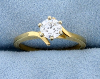 Op de afbeelding: Een gouden ring met een enkele ronde diamant in een kraalbezetting. De band is gebogen en heeft een delicaat ontwerp.