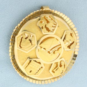 May include: A gold-colored pendant with a circular design. The pendant features a central circle surrounded by five hexagonal shapes, each with intricate cut-out designs. The outer edge has a beaded border, and a small loop is at the top for a chain.