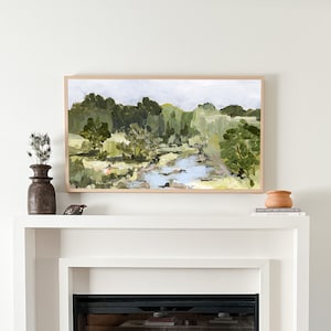 May include: A framed painting depicting a landscape with a river winding through a woodland. The artwork is rendered in shades of green, blue, and brown. The painting is hung on a white wall above a white fireplace.