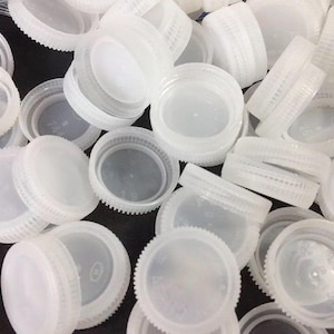 May include: A pile of white plastic bottle caps. The caps are all the same size and shape, and they are arranged in a random pattern.