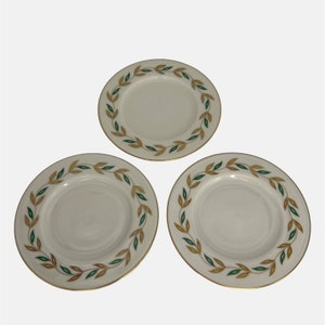 Può includere: Tre piattini in ceramica bianca con bordo dorato e un design a foglie verdi e dorate.