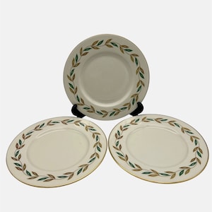 Puede incluir: Tres platos de cerámica blanca con borde dorado y diseño de hojas verdes y marrones.