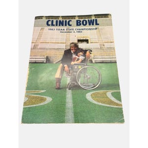 May include: A vintage program for the 1983 TSSAA State Championship "Clinic Bowl" held on December 3, 1983. The cover features a photo of a man and a child in a wheelchair on a football field.