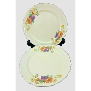 May include: Two white ceramic dinner plates with a floral design. The plates have a scalloped edge and a gold trim. The flowers are orange, purple, and yellow.