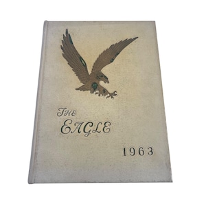 May include: Vintage yearbook titled "The Eagle" from 1963. The cover features a detailed illustration of a brown eagle with outstretched wings. The title is in elegant script, and the year is printed below.