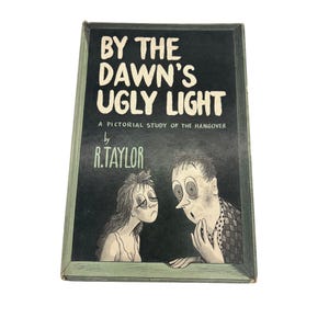 May include: Vintage book titled "By the Dawn's Ugly Light" by R. Taylor. The cover features a black background with white text and a cartoon illustration of two people with exaggerated expressions. The book is a pictorial study of the hangover.