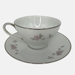 May include: A white teacup and saucer set with a delicate pink rose floral design and a silver rim.