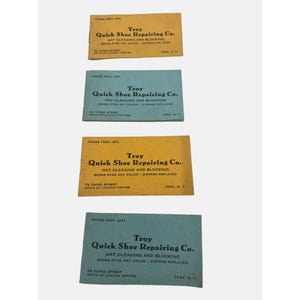 May include: Four vintage business cards for Troy Quick Shoe Repairing Co. The cards are yellow and blue with black text. The text on the cards reads "Troy Quick Shoe Repairing Co. Hat Cleaning and Blocking Shoes Dyed Any Colour - Zippers Replaced 79 Third Street South of Lincoln Theatre Troy, N.Y."