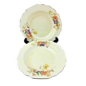 May include: Two white ceramic soup bowls with a floral design. The bowls have a scalloped edge and are decorated with orange, yellow, and purple flowers.