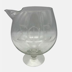 May include: A clear glass pitcher with a wide base and a spout. The pitcher is etched with the Greek letters "ΣΦΕ".