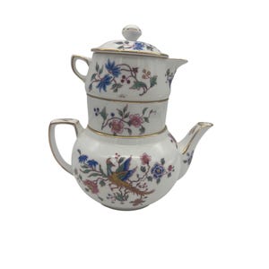 May include: A white porcelain teapot with a stacked design. The teapot is decorated with colorful floral and bird motifs, accented with gold trim. The teapot has a lid and a spout.