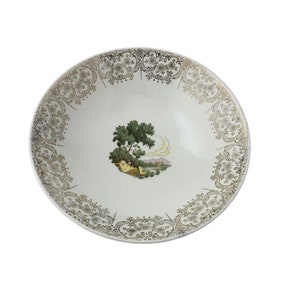 Puede incluir: Un tazón de cerámica blanca con un patrón de encaje dorado y negro alrededor del borde. El centro del tazón presenta una escena de paisaje verde y marrón.