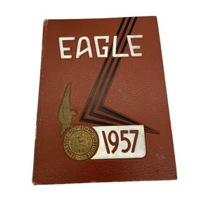 May include: A brown leather-bound yearbook with the word "EAGLE" in white lettering on the front cover. The year "1957" is printed in white on a white and black background. A gold seal with the text "Tennessee Polytechnic Institute 1915" is on the bottom left corner of the cover.