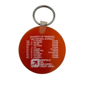 May include: Orange keychain with a silver ring. The keychain features the text "UNIVERSITY OF TENNESSEE 1983 FOOTBALL SCHEDULE" and the TVA Employees Credit Union logo. The schedule lists football games.