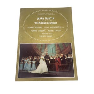 Puede incluir: Un programa vintage de la obra musical "The Sound of Music" con Mary Martin. La portada es de color dorado descolorido con el título y los nombres del elenco en blanco. La parte inferior muestra una escena de la obra.