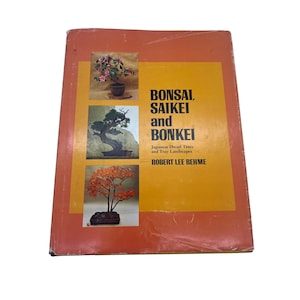 May include: A book titled "Bonsai, Saikei and Bonkei" by Robert Lee Behme. The cover is orange with a yellow rectangle containing images of bonsai trees. The book is wrapped in clear plastic.