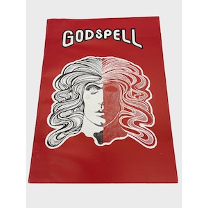 May include: A red program for the musical "Godspell" featuring a black and white illustration of a woman's face.
