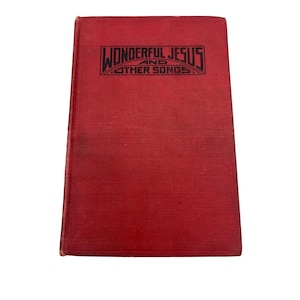 Pode incluir: Um livro vintage com capa vermelha. O título "Wonderful Jesus and Other Songs" está impresso em letras pretas e estilizadas na parte superior. O livro tem uma aparência desgastada, sugerindo idade e uso. A capa é de cor vermelha sólida.