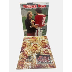 May include: Two Wolfpack News game day programs for the NC State vs. Duke football game. The front cover features a photo of a woman and a man in a red and white football uniform. The back cover features a photo of the NC State football team in their red and white uniforms.