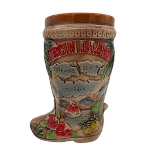 May include: A brown ceramic mug shaped like a boot with a map of the Virgin Islands on the front. The mug has the words "Virgin Islands" in red lettering and the names of the islands "St. Thomas", "St. John", and "St. Croix" in black lettering.