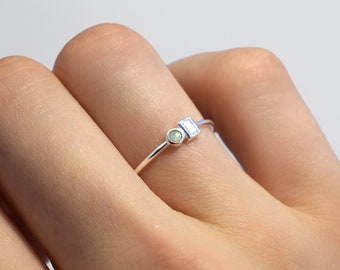 May include: A silver ring with a small, round opal gemstone and a larger, rectangular clear gemstone.