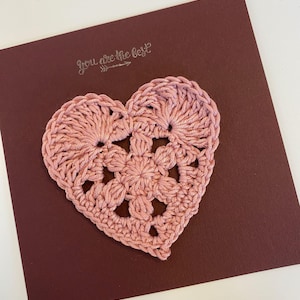 Peut inclure: Un cœur en crochet rose avec un message qui dit "You are the best" sur une carte marron.