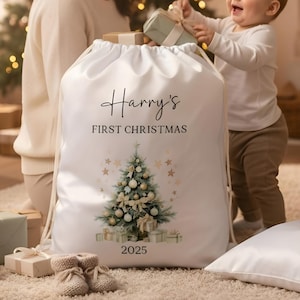 May include: A white drawstring Christmas sack with the text "Harry's FIRST CHRISTMAS" and the year 2025. The sack features a watercolor Christmas tree design with gold stars and wrapped gifts. A baby is reaching for a gift.