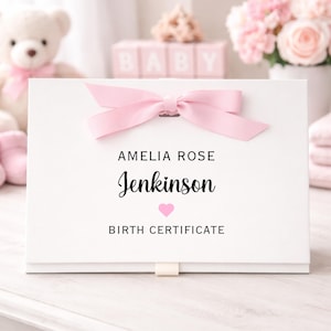 May include: A white rectangular box tied with a pink ribbon bow. The box has the name "Amelia Rose Jenkinson" and the words "Birth Certificate" printed in black. A pink heart is below the name.