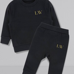 May include: Black baby tracksuit with gold embroidered initials "LW" on the sweatshirt and pants.