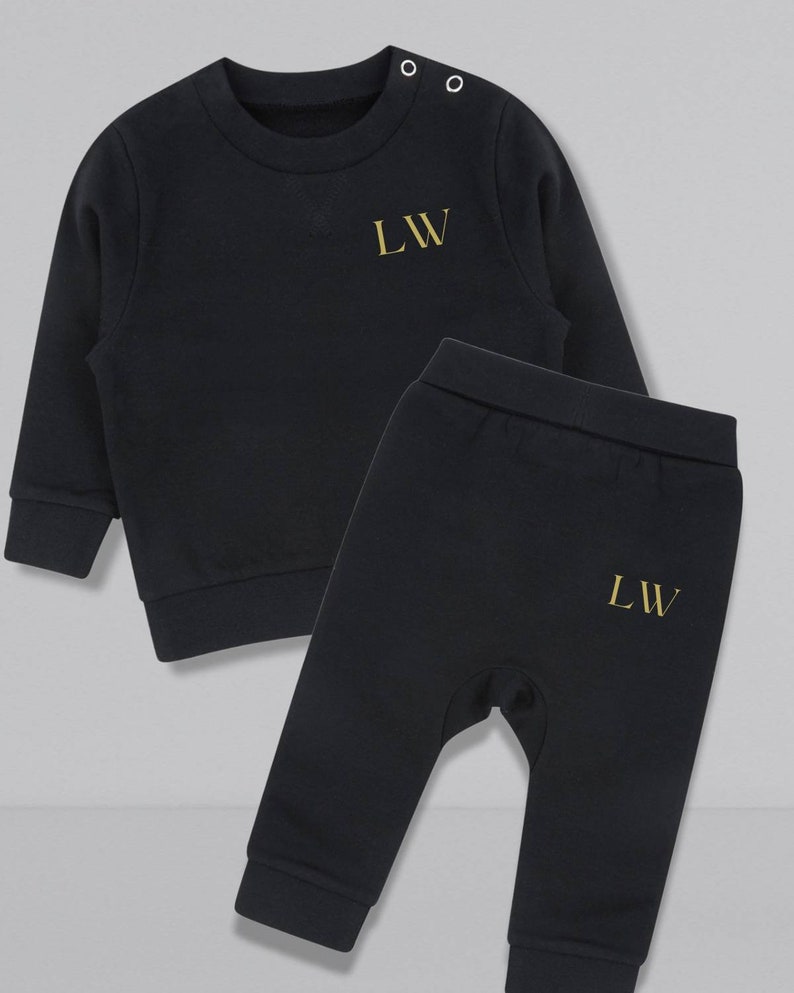 May include: Black baby tracksuit with gold embroidered initials "LW" on the sweatshirt and pants.