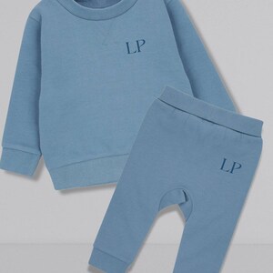 May include: A blue baby sweatshirt and matching pants set with the initials "LP" embroidered on both pieces.