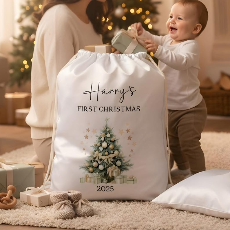 May include: A white drawstring Christmas sack with the text "Harry's FIRST CHRISTMAS" and the year 2025. The sack features a watercolor Christmas tree design with gold stars and wrapped gifts. A baby is reaching for a gift.