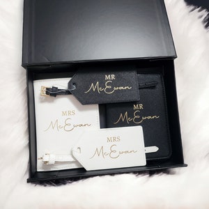 Op de afbeelding: Twee zwarte paspoorthouders met gouden opschrift "MR McEwan" en "MRS McEwan". Twee witte bagagelabeltjes met gouden opschrift "MRS McEwan" en "MR McEwan".