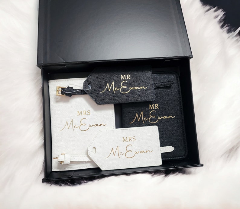 Op de afbeelding: Twee zwarte paspoorthouders met gouden opschrift "MR McEwan" en "MRS McEwan". Twee witte bagagelabeltjes met gouden opschrift "MRS McEwan" en "MR McEwan".