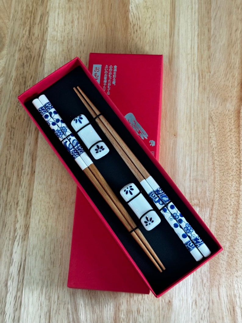 May include: A set of wooden chopsticks with blue and white floral designs, packaged in a red box with Japanese text that reads "お箸" which means "chopsticks".