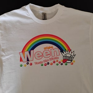 Puede incluir: Camiseta blanca con un arcoíris, la palabra "Ween" en letras rojas, y los textos "Original" y "Taste The Waste" en letras amarillas. Una cara de dibujos animados con la lengua fuera está por encima del texto "Taste The Waste".