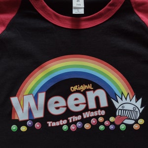 May include: Black and red baseball tee shirt featuring a rainbow arc and the words "Original Ween Taste The Waste" in white lettering. The graphic also includes a cartoon character with a tongue sticking out and a row of colourful "W"s.