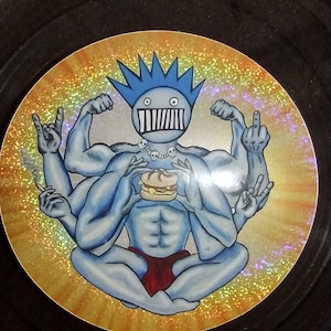 May include: A blue, multi-armed figure with a spiky blue mohawk sits in a meditative pose. The figure has a toothy grin and is holding a hamburger. The background is a yellow and orange gradient with a glittery texture.
