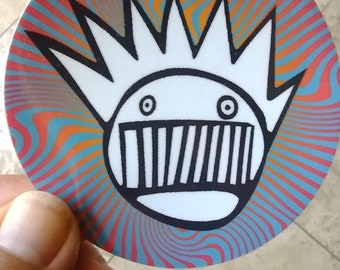 May include: A white sticker with a black and white cartoon character with a spiky hairdo and a mouth with teeth. The background is a swirling pattern of red, orange, blue, and green.