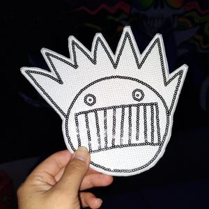 May include: White iron-on patch with a black outline of a cartoon face with a mohawk and a mouth with teeth.