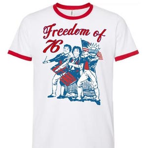 May include: A white ringer t-shirt with red trim on the collar and sleeves. The front features a red and blue graphic of three figures with drums and an American flag, with the text Freedom of 76 printed in red script above the illustration.