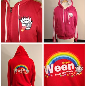 May include: Red zip-up hoodie with white drawstrings and a white-lined hood. The front features a cartoon graphic and the word "Ween" with a rainbow design. The back of the hoodie also displays the "Ween" logo and rainbow.