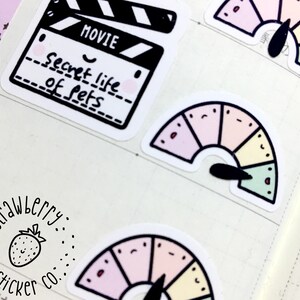 May include: A set of colorful stickers featuring a movie clapperboard with the text "Secret Life of Pets" and a rainbow-colored gauge with a black needle.