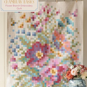 May include: A beige quilt with a pixelated floral design in shades of pink, red, blue, green, and yellow. The quilt is hanging on a white wall and has the text "Tilda's Chambray Basics Flower Branch Embroidery Quilt" at the top.