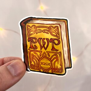 Puede incluir: Una pegatina que representa un libro estilizado con las letras "RWP" en la portada. El libro tiene una cubierta amarilla con ribetes marrones y adornos decorativos. La pegatina se sostiene sobre un fondo blanco.