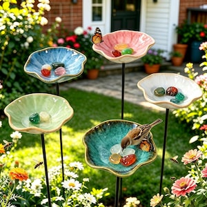Puede incluir: Cinco estacas de jardín con forma de flor y bordes festoneados en azul, rosa, blanco, verde claro y cerceta. Cada cuenco contiene piedras pulidas lisas y coloridas. Un pequeño pájaro marrón se posa en el cuenco cerceta y hay dos mariposas.