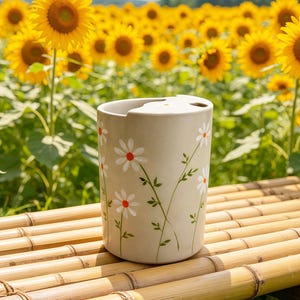 Peut inclure: Un porte-brosse à dents en céramique beige avec un motif floral de marguerites. Le support a un dessus incurvé avec deux ouvertures et est décoré de marguerites blanches à centres rouges et tiges vertes. Le fond présente un champ de tournesols.